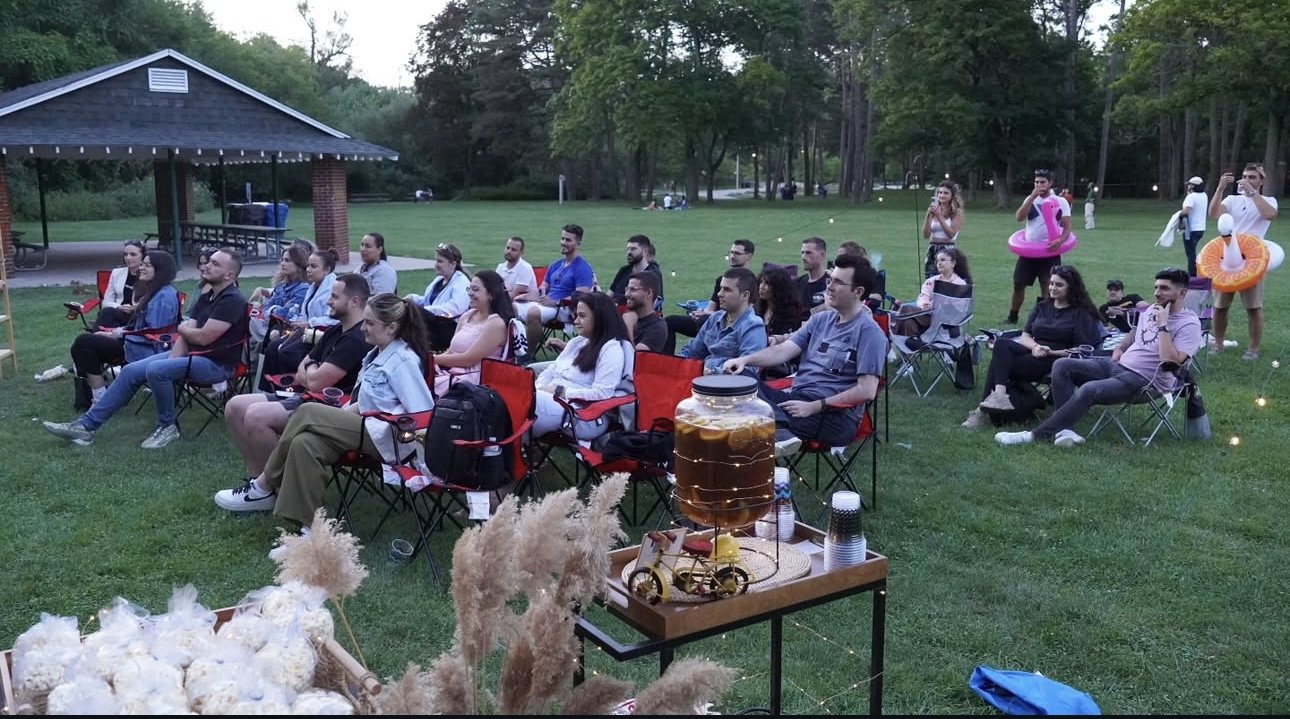 A community audience seated outdoors for an Albanian Youth movie night in a Toronto park