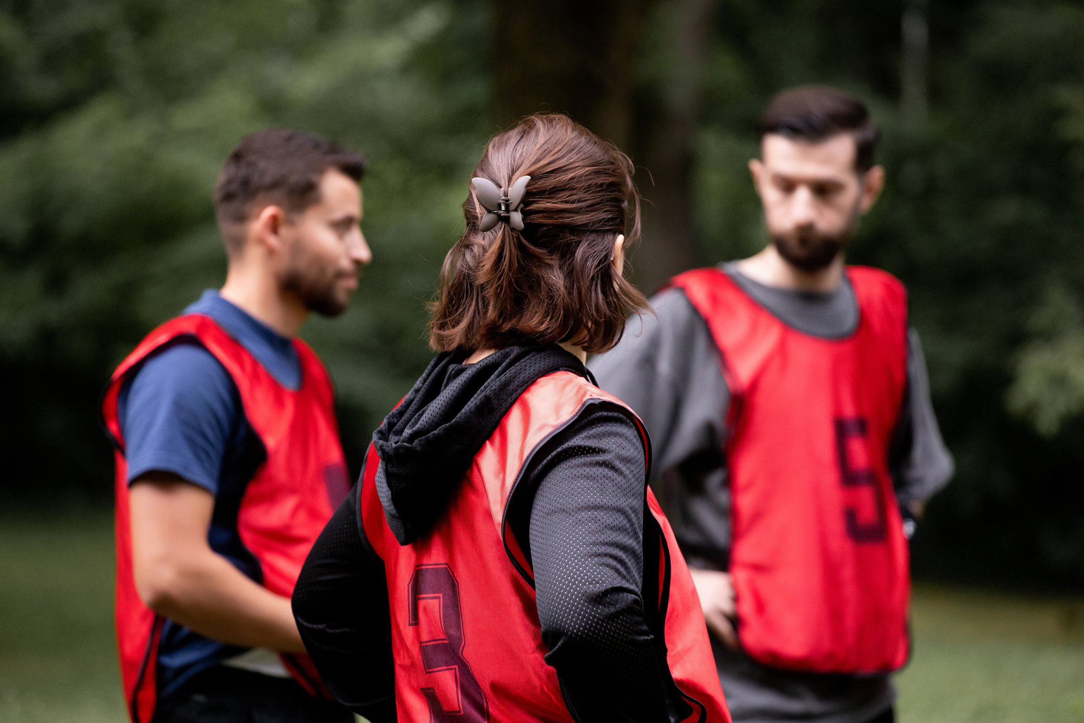 Three adults in red sports bibs talking during an outdoor Albanian Youth volleyball activity
